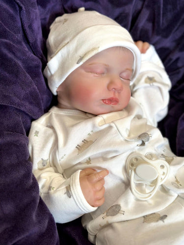 A baby doll rests on a soft blanket, showcasing its delicate features and clothing.